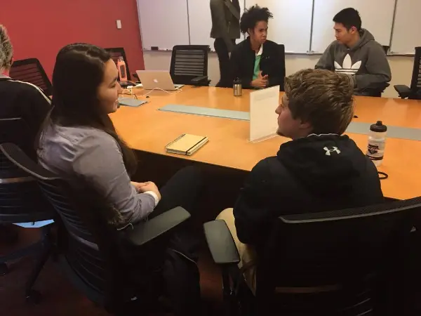 students sit around a tablet, talking