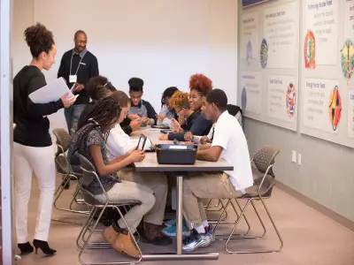Volunteers walking around the room while students work on their tablets