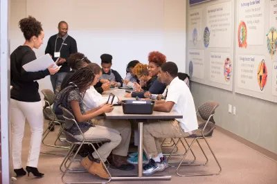 Volunteers walking around the room while students work on their tablets